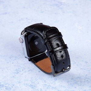 K&ouml;nnte beinhalten: Schwarzes Lederarmband mit silberner Schlie&szlig;e. Das Armband ist f&uuml;r eine Smartwatch mit schwarzem Bildschirm konzipiert.