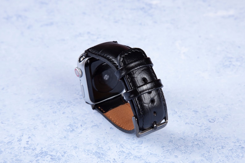 K&ouml;nnte beinhalten: Schwarzes Lederarmband mit silberner Schlie&szlig;e. Das Armband ist f&uuml;r eine Smartwatch mit schwarzem Bildschirm konzipiert.