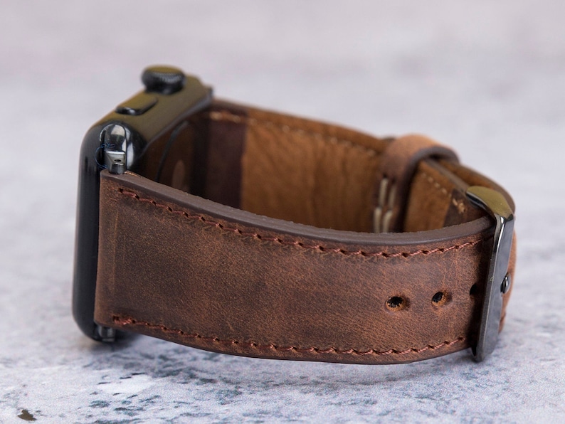 May include: A brown leather watch strap with a black metal buckle. The strap is stitched with brown thread and has a distressed look.
