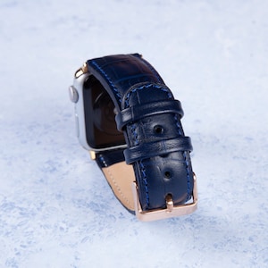 K&ouml;nnte beinhalten: Ein dunkelblaues Lederarmband mit einer ros&eacute;goldenen Schlie&szlig;e und blauen N&auml;hten. Das Armband ist f&uuml;r eine Smartwatch konzipiert.