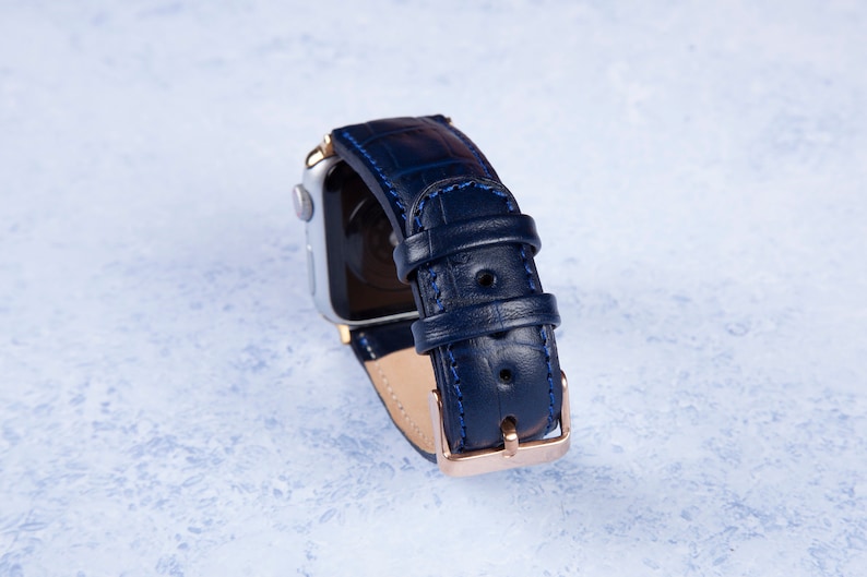 K&ouml;nnte beinhalten: Ein dunkelblaues Lederarmband mit einer ros&eacute;goldenen Schlie&szlig;e und blauen N&auml;hten. Das Armband ist f&uuml;r eine Smartwatch konzipiert.
