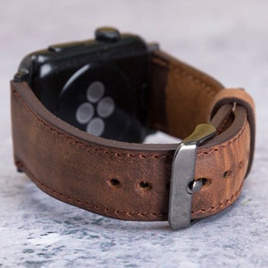 May include: A brown leather watch strap with a silver buckle. The strap is designed for an Apple Watch.