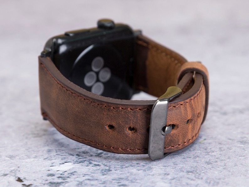 May include: A brown leather watch strap with a silver buckle. The strap is designed for an Apple Watch.