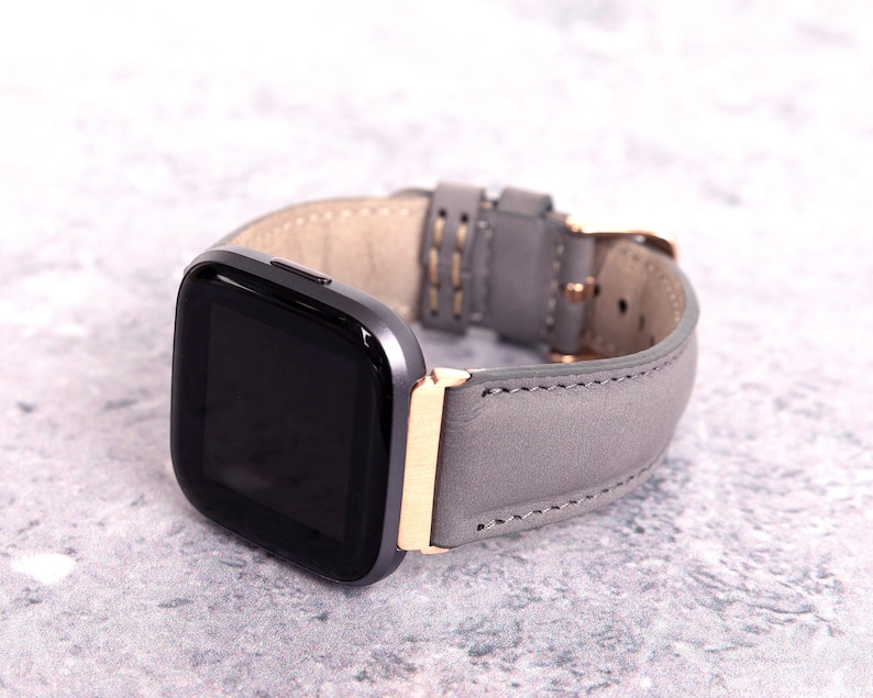 May include: A gray leather watch band with a gold buckle and a black smartwatch face.
