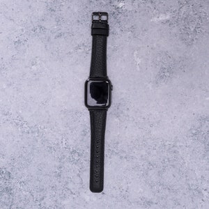 May include: A black leather watch band with a black Apple Watch face.