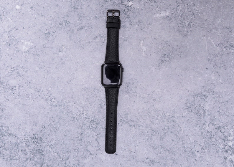 May include: A black leather watch band with a black Apple Watch face.