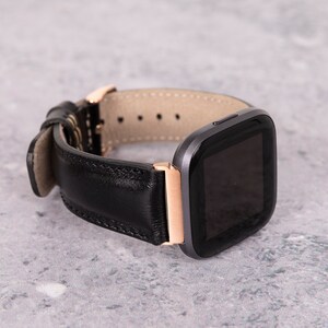 May include: A black leather watch band with a rose gold buckle and a black smartwatch face.