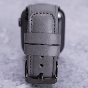 May include: A gray leather watch band with a silver buckle. The band is designed for a smartwatch.