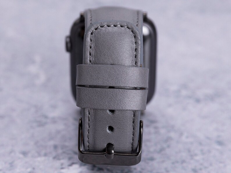 May include: A gray leather watch band with a silver buckle. The band is designed for a smartwatch.