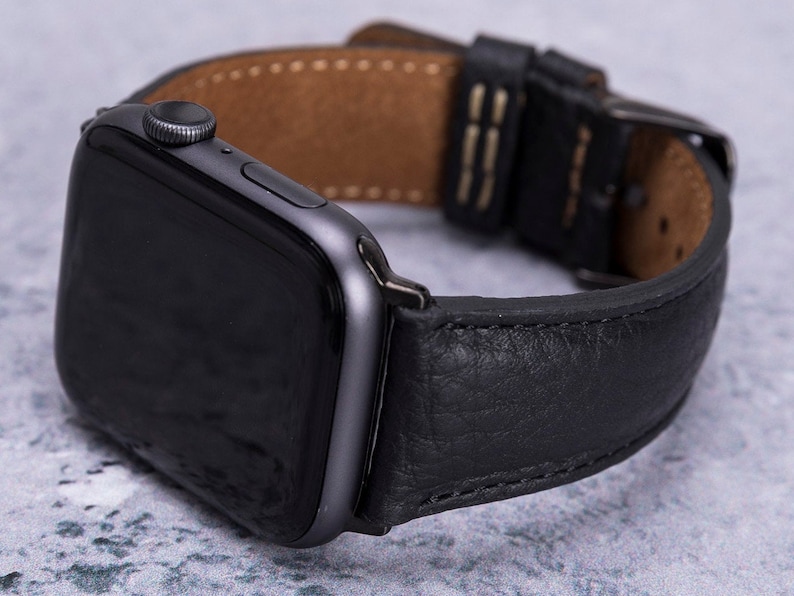 以下が含まれることがあります： 黒いApple Watchに黒い革製の腕時計バンド。バンドはダブルステッチのデザインで、裏地は茶色の革製です。