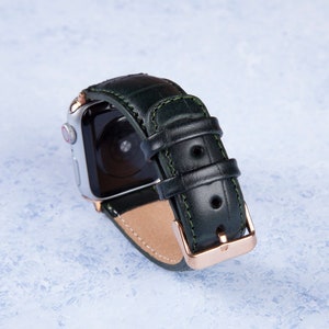 K&ouml;nnte beinhalten: Ein dunkelgr&uuml;nes Lederarmband mit einer ros&eacute;goldenen Schlie&szlig;e. Das Armband ist f&uuml;r eine Smartwatch konzipiert und hat einen gen&auml;hten Rand.