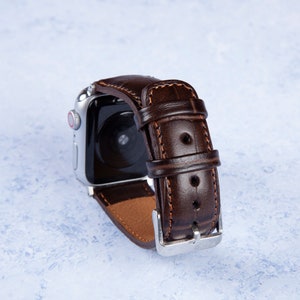 K&ouml;nnte beinhalten: Ein braunes Lederarmband mit einer silbernen Schlie&szlig;e. Das Armband ist f&uuml;r eine Smartwatch konzipiert und hat einen gen&auml;hten Rand.