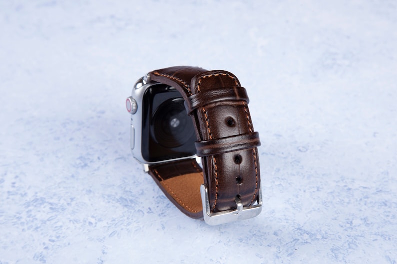 K&ouml;nnte beinhalten: Ein braunes Lederarmband mit einer silbernen Schlie&szlig;e. Das Armband ist f&uuml;r eine Smartwatch konzipiert und hat einen gen&auml;hten Rand.