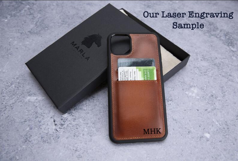 May include: A brown leather phone case with a card slot and a black border. The case has the initials "MHK" engraved on the back. The case is shown next to a black box with the word "MARLA" printed on it.