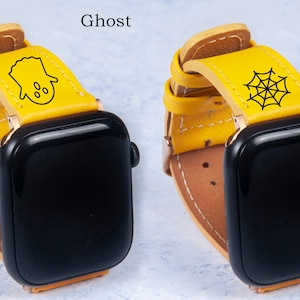 Könnte beinhalten: Zwei gelbe Lederarmbänder für Apple Watch mit unterschiedlichen Designs. Das Armband links hat ein Geisterdesign, das Armband rechts ein Spinnennetzdesign. Beide Armbänder sind auf einer schwarzen Apple Watch zu sehen.