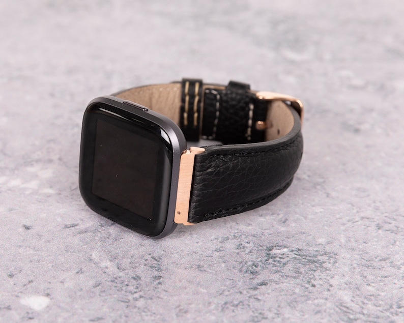 May include: A black leather watch band with a rose gold buckle and a black smartwatch face.