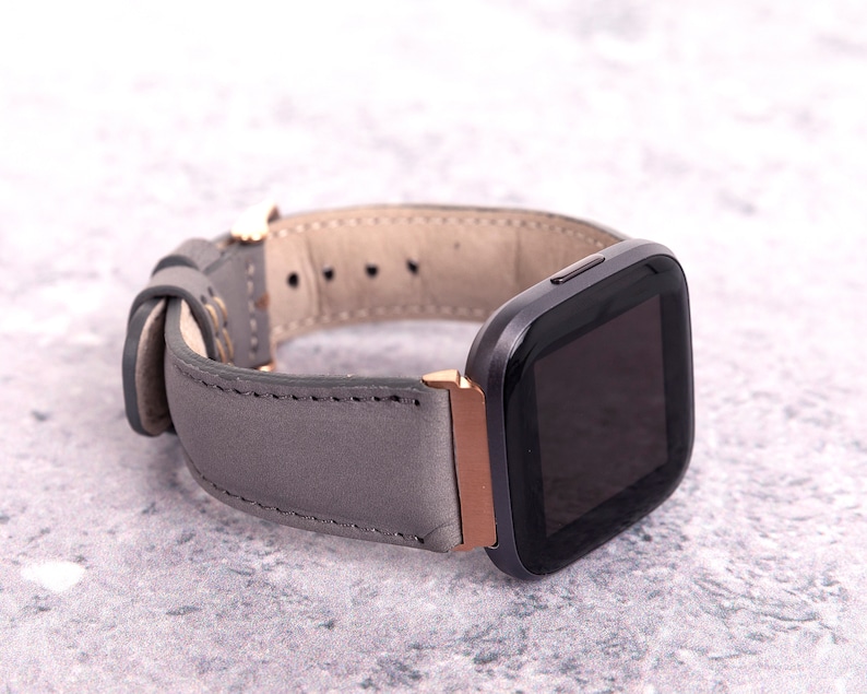 May include: A gray leather watch band with a rose gold buckle and a black smartwatch face.