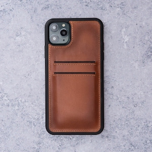 May include: A brown leather phone case with a black border and a built-in card holder. The case has a cutout for the phone's camera lens.