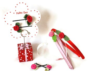 May include: A display of handmade hair accessories, including red and pink rose-adorned headbands and bobby pins. A white flower-shaped display with the text "Polka Dot" holds bobby pins. The display sits on a red polka dot gift box.
