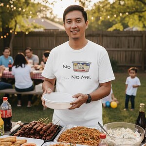 May include: A man wearing a white t-shirt with the text "No Baon... No Me" and a graphic of a food container. He is holding a white bowl, with a table of food in front of him. Other people are in the background.