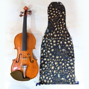 Puede incluir: Un violín de madera marrón con una funda de violín de estampado de leopardo negro y dorado. La funda tiene un diseño de ojo azul y blanco.