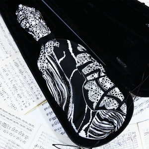 Puede incluir: Una funda de violín con estampado en blanco y negro con cierre de cremallera. La funda está abierta y el interior está forrado con tela negra.