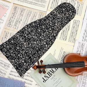 Puede incluir: Una funda de violín de tela floral en blanco y negro con un violín y partituras en el fondo. La partitura presenta el texto "J.S. Bach Suite III C Major BWV 1009 for Violoncello and Klavier Robert Schumann"