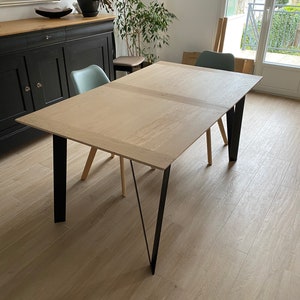 Peut inclure: Une table à manger en bois clair avec des pieds en métal noir. La table est rectangulaire et a un design simple.