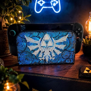 Könnte beinhalten: Eine schwarze Handheld-Spielkonsole mit einer blau-weiß gemusterten Hülle mit einem stilisierten Design. Die Hülle befindet sich auf einer Holzoberfläche, mit einer neonblauen Controller-Umrisslinie im Hintergrund. Das Gesamtthema ist Gaming.