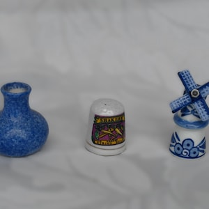 Può includere: Una collezione di figurine in ceramica in miniatura. Include un vaso blu maculato, un ditale con un design colorato e un mulino a vento blu e bianco. Le figurine sono piccole e dettagliate.
