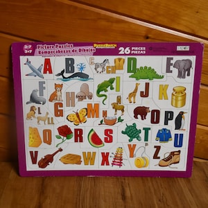 Puede incluir: Un rompecabezas de alfabeto colorido con 26 piezas. Cada letra está emparejada con una imagen, como una mariposa, un avión, una jirafa y una sandía. El rompecabezas está hecho de cartón resistente y es perfecto para los jóvenes estudiantes.