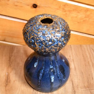May include: A handcrafted ceramic vase with a unique two-part design. The top section is a textured, spherical shape with a small opening, while the base is a rounded, elongated form. The vase features a dark blue glaze with gold accents.