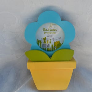 May include: A wooden Easter-themed photo frame shaped like a flower in a yellow pot. The flower is light blue with green leaves and holds a circular photo space. The text "It's Easter for keepsake" is visible.