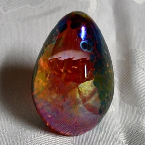 May include: A glass egg ornament with iridescent colors, including red, orange, yellow, blue, and green. The egg has a speckled pattern and a glossy finish.