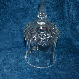 May include: A clear glass bell with a diamond pattern and a tall handle. The bell is sitting on a blue surface.