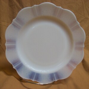 May include: A white milk glass dinner plate with a scalloped edge and a purple and white design.
