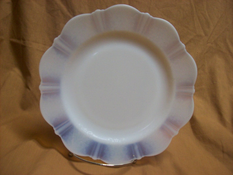 May include: A white milk glass dinner plate with a scalloped edge and a purple and white design.