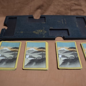 May include: Four cards with a yellow border and a black and white image of a mountain scene with a lake and trees. The cards are arranged in a row on a brown surface. The cards are from a game called "Mt. Fuji"