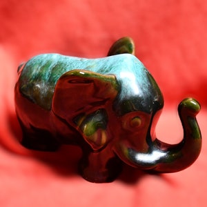 May include: A ceramic elephant figurine with a green and black glaze. The elephant has a long trunk and large ears.