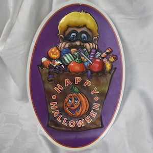 Puede incluir: Decoración ovalada de Halloween con un niño de dibujos animados con máscara, mirando por encima de una bolsa marrón llena de caramelos y calabazas. La bolsa tiene las palabras "Happy Halloween" alrededor de una calabaza sonriente.