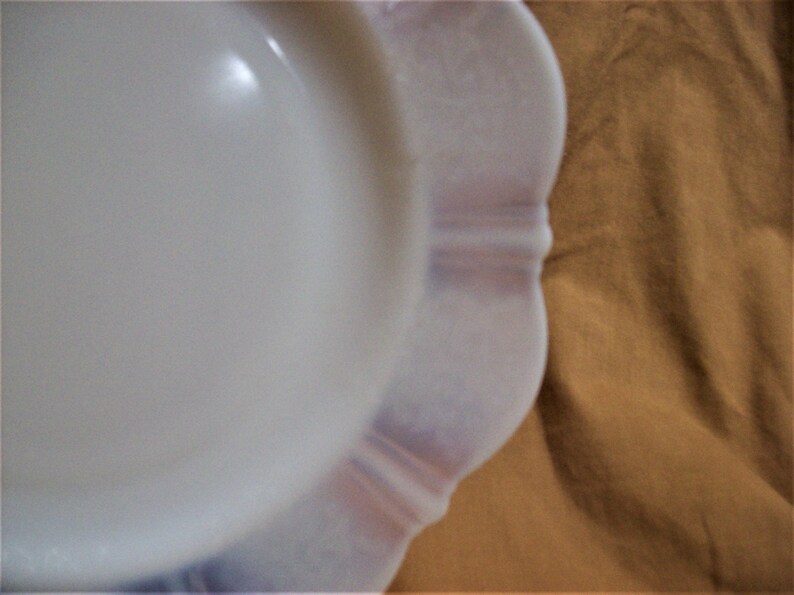 May include: A white milk glass plate with a scalloped edge. The plate has a subtle pink hue and is perfect for serving desserts or appetizers.