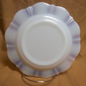 May include: A white milk glass plate with a scalloped edge and a purple rim. The plate is on a stand.