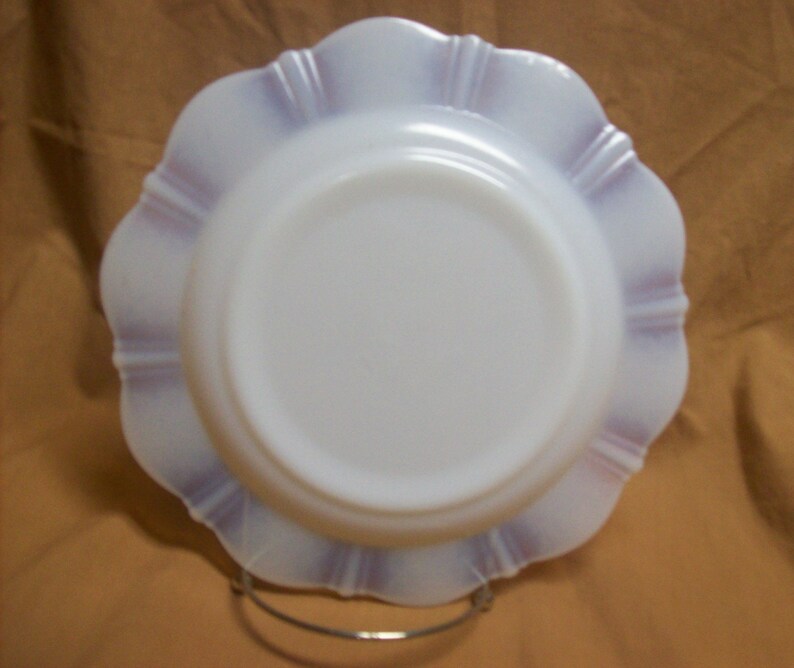 May include: A white milk glass plate with a scalloped edge and a purple rim. The plate is on a stand.