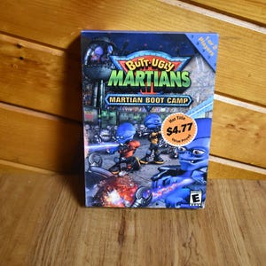 May include: A video game box for "Butt-Ugly Martians: Martian Boot Camp" featuring blue alien characters in a futuristic setting. The box has a "Hot Title" sticker and indicates it's for 1 or 2 players.