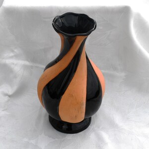 May include: A decorative vase featuring a swirling, twisted design with alternating vertical bands of glossy black and matte terracotta-colored clay. The vase has a bulbous body, a narrow neck, and a ruffled, scalloped rim with a circular base.