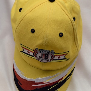 Puede incluir: Gorra de béisbol amarilla con un logotipo de Justice Bros. Qualifiers en blanco y negro y detalles rojos y negros en la visera.