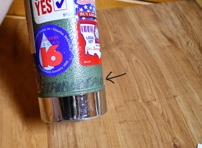May include: A cylindrical metal object with a green textured body and a shiny silver base. The object has several stickers, including one for Local Union 16, Omaha, Nebraska, and another with the text "BUY AMERICAN".