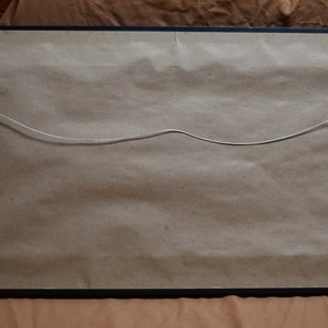 May include: The back of a framed picture with a brown paper backing and a wire hanger attached. The frame is black.