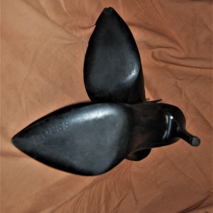 May include: A pair of black leather heeled boots with pointed toes. The boots are shown from the bottom, with the soles facing the camera.