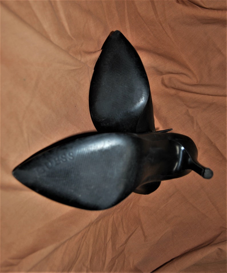May include: A pair of black leather heeled boots with pointed toes. The boots are shown from the bottom, with the soles facing the camera.